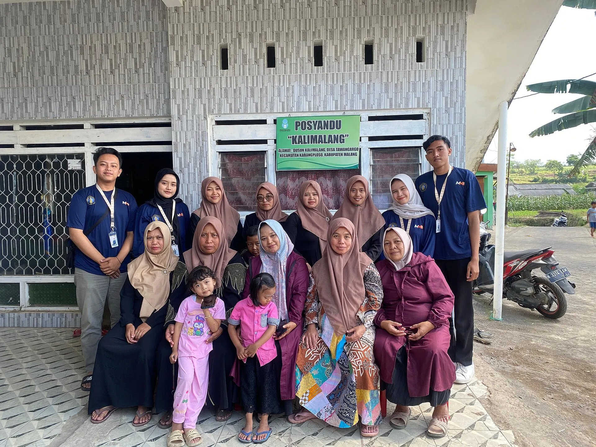 Foto contoh: ibu-ibu berkerudung dan anak-anak berfoto bersama sambil tersenyum di depan sebuah bangunan.
