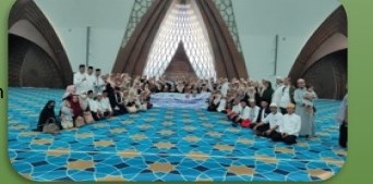 Foto dokumentasi: jamaah duduk berbaris di lantai karpet biru bermotif di dalam masjid besar berkubah tinggi.
